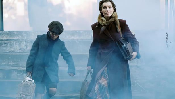 Eine Frau in einem Mantel mit Pelzkragen und ein Junge steigen eine Treppe im Nebel hinunter.