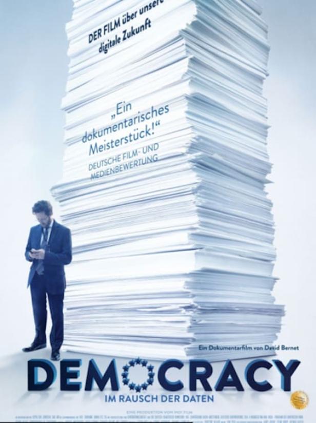 Das Filmplakat für „Democracy – Im Rausch der Daten“ zeigt einen Mann vor einem riesigen Papierstapel.