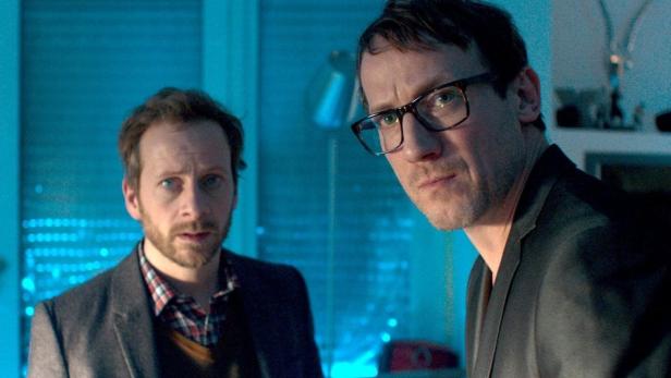 Zwei Männer stehen in einem Raum mit blauer Beleuchtung.