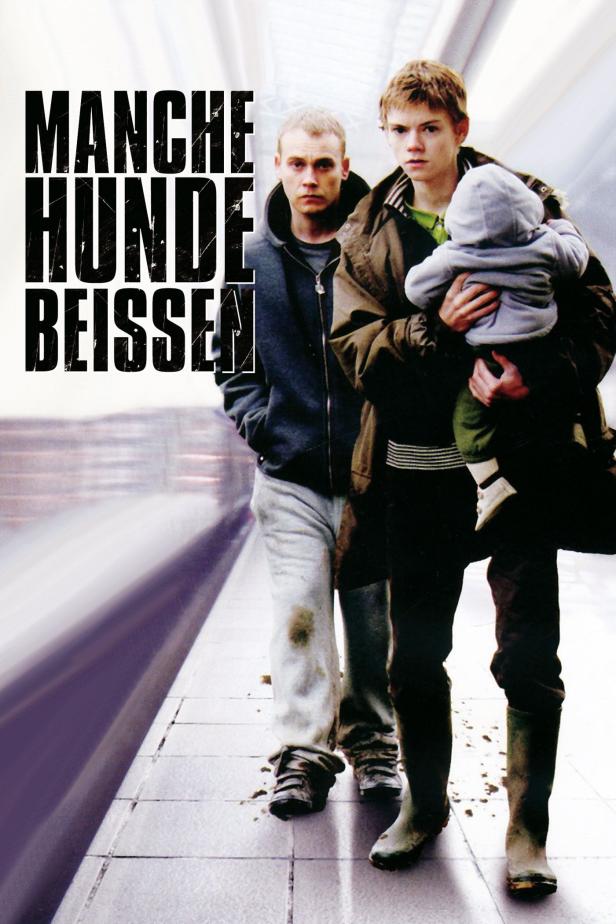 Das Filmplakat für „Manche Hunde beißen“ zeigt zwei Männer und ein Baby auf einem Bahnsteig.