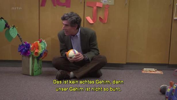 Ein Mann sitzt auf dem Boden und hält ein buntes Gehirnmodell in den Händen.