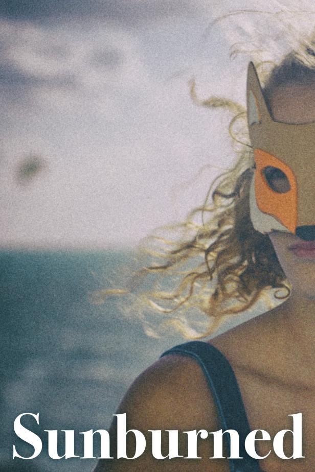 Eine Person mit lockigem Haar trägt eine Fuchsmaske am Strand.