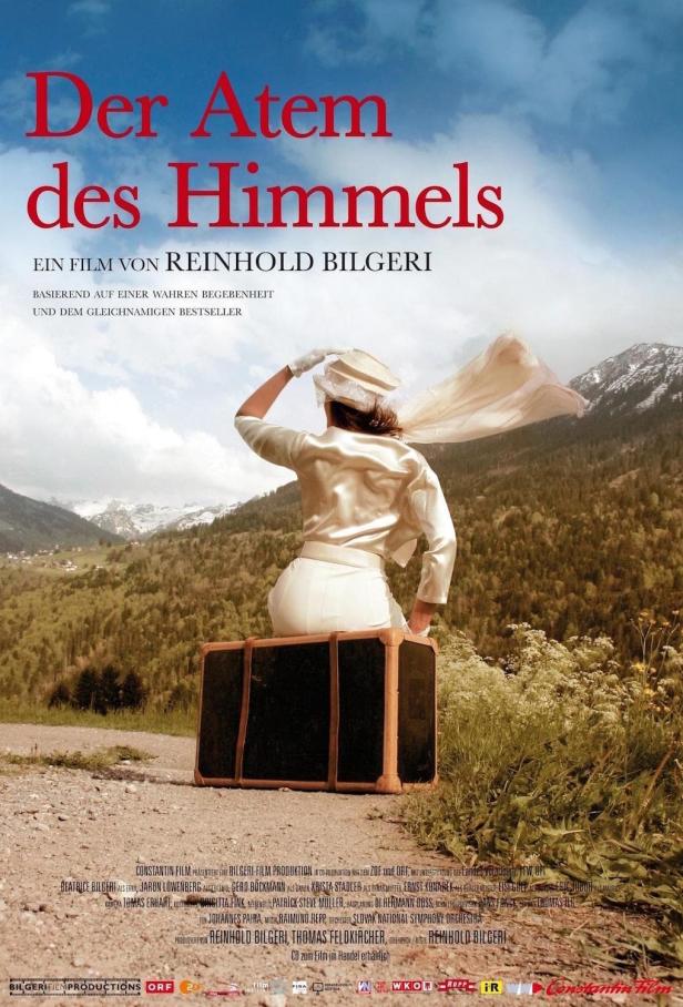 Das Filmplakat für „Der Atem des Himmels“ zeigt eine Frau auf einem Koffer vor Bergkulisse.
