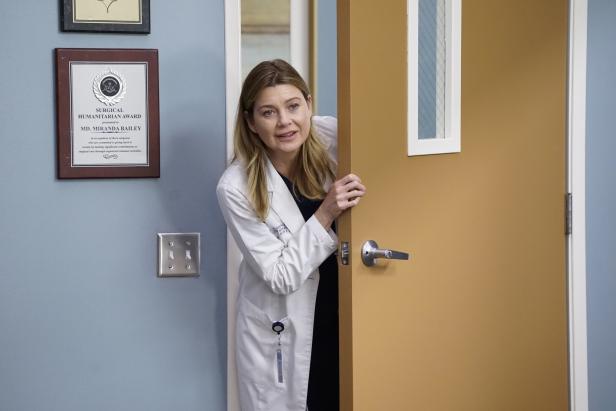 Eine blonde Ärztin trägt einen Kittel und schaut in ein Zimmer, mit der Tür halb offen.