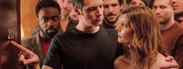 Ein Paar steht vor einer Tür mit der Nummer 212, umgeben von anderen Menschen.