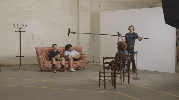 Zwei junge Schauspieler sitzen auf einem Sofa während eines Drehs.