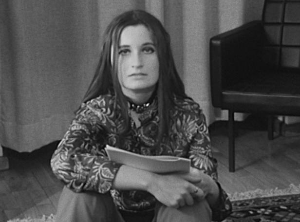 Eine junge Frau sitzt mit einem Buch in der Hand auf dem Boden.