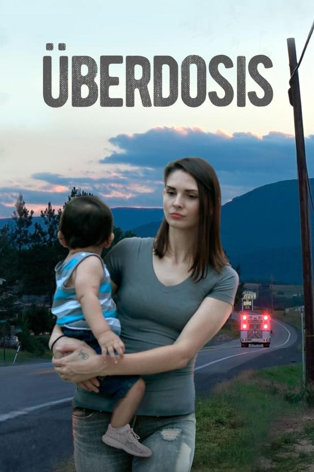 Eine Frau hält ein Kind im Arm, während ein Krankenwagen auf der Straße fährt.