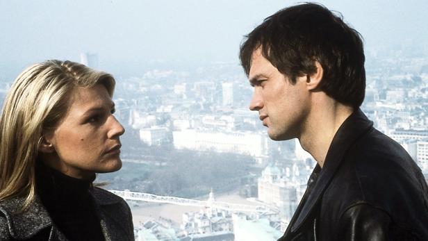 Eine Frau und ein Mann stehen vor einer verschwommenen Stadtlandschaft.