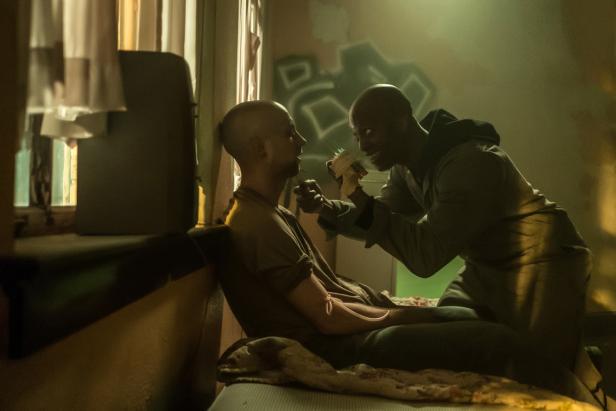 Ein Mann injiziert einem anderen Mann in einem heruntergekommenen Raum eine Substanz.