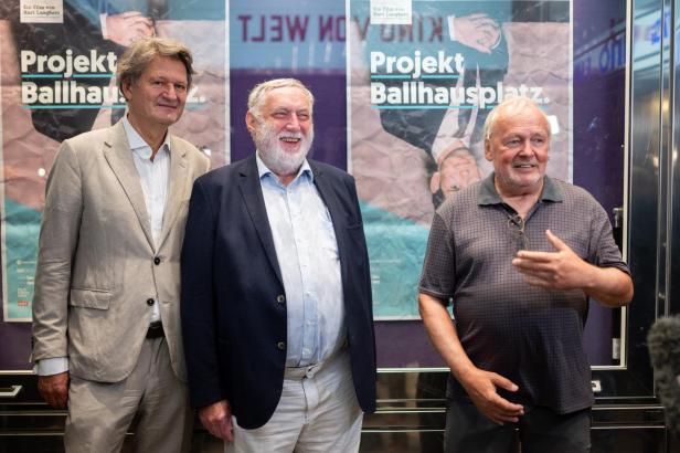 Drei Männer posieren vor einem Plakat für „Projekt Ballhausplatz“.