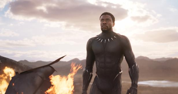 Chadwick Boseman als Black Panther vor einem brennenden Flugzeugwrack.
