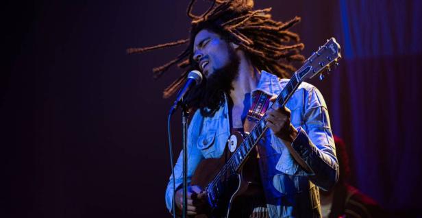 Bob Marley mit wehenden Rastalocken und Gitarre am Mikro auf einer Bühne