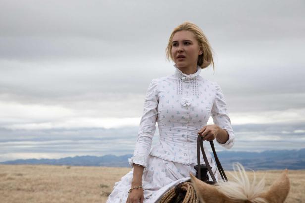 Eine blonde Frau sitzt in einem weißen Kleid auf einem Pferd