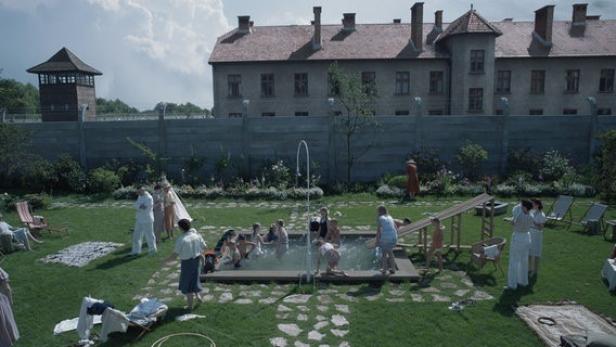 Familie Höss genießt einen Sommertag an ihrem Brunnen in ihrem idyllischen Garten. Im Hintergrund das KZ Auschwitz.