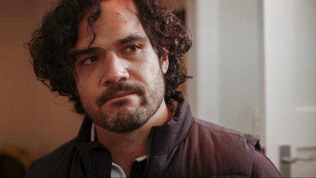 Ein Mann mit dunklen Locken und Bart trägt eine Weste.