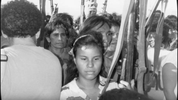 Eine Menschenmenge, einige tragen Gewehre, in einer Schwarzweißaufnahme.