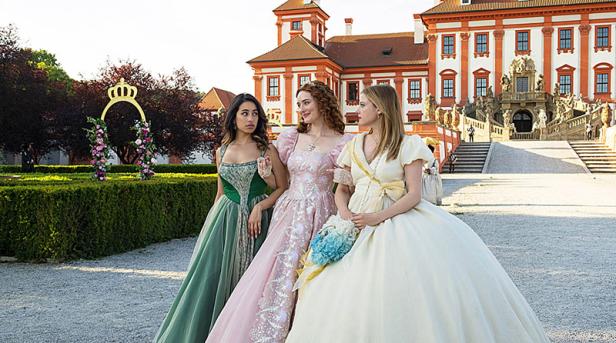 Drei Prinzessinen laufen in Prinzessinnen-Kleidern in einem Schlossgarten entlang. Im Hintergrund ist das rot-weiße Schloss zu sehen.