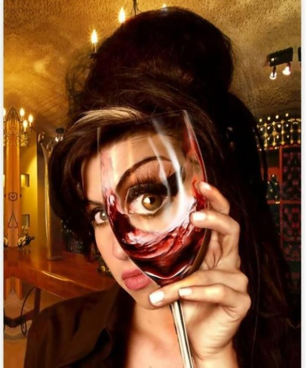 Eine Frau hält ein Weinglas vor ihr Gesicht, sodass ein Auge durch den Wein sichtbar ist.