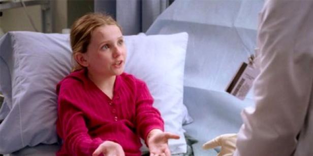 Abigail Breslin als blondes Mädchen in pinken Klamotten in einem Krankenhausbett.