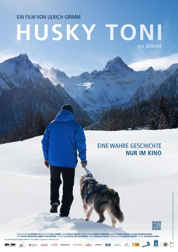 Ein Mann und ein Husky wandern im Schnee vor einer Bergkulisse.