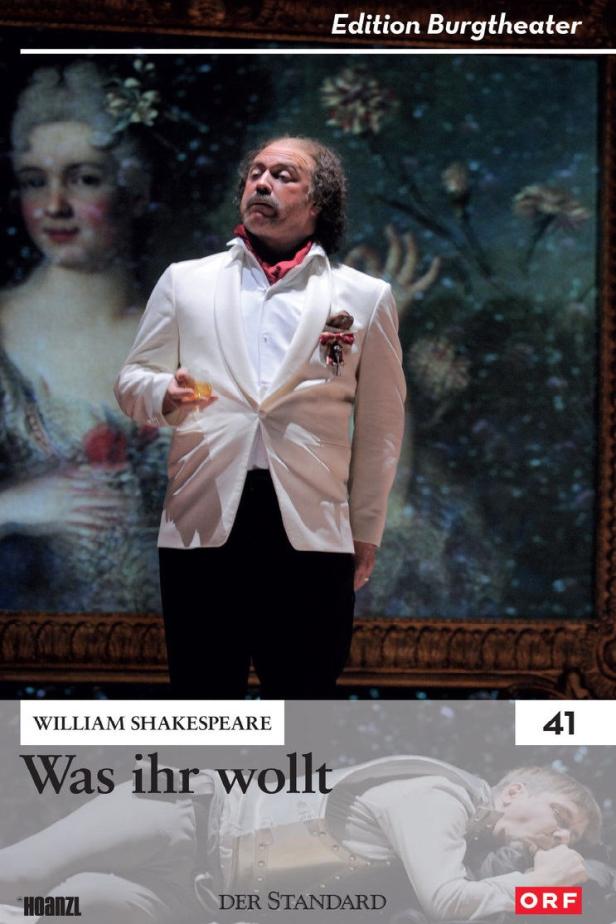 Ein Schauspieler in weißem Anzug steht vor einem Bühnenbild für „Was ihr wollt“.