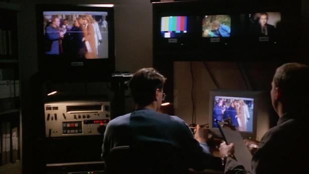 Zwei Männer sitzen in einem dunklen Raum vor mehreren Monitoren und bearbeiten Videomaterial.