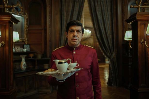 Ein Hotelpage in roter Uniform serviert Tee und Gebäck.