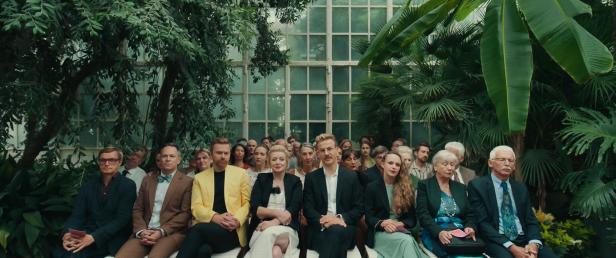 Eine Gruppe von Menschen sitzt in einem Gewächshaus und schaut zu.