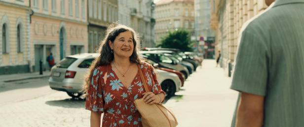 Eine Frau mit einem geblümten Kleid und einer Tasche auf einer sonnigen Straße.