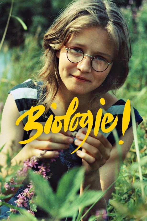 Ein junges Mädchen mit Brille hält eine kleine Blume in der Hand, im Vordergrund steht das Wort „Biologie!“.