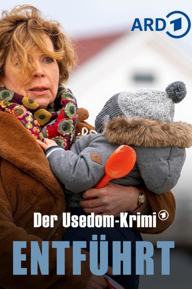 Eine Frau hält ein Kind mit einer orangefarbenen Schaufel im Arm, Plakat für „Der Usedom-Krimi: Entführt“.