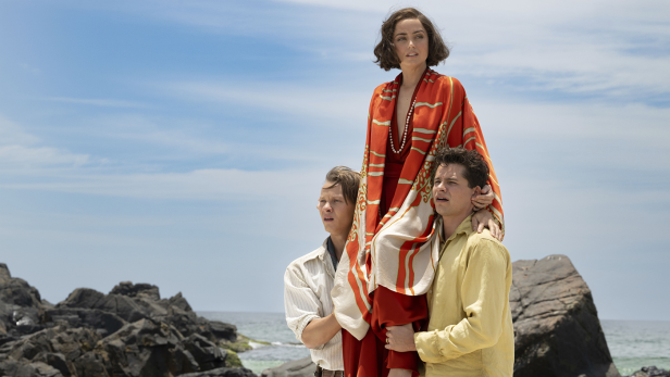 Ana de Armas steht auf den Schultern zweier Männer am Strand.