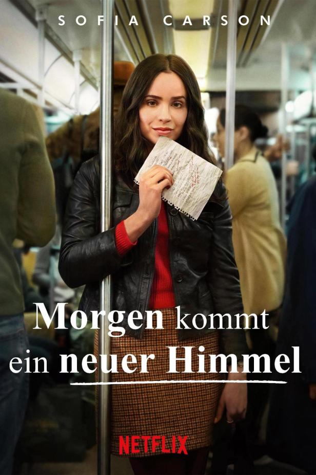 Sofia Carson hält ein Blatt Papier in der Hand, im Hintergrund eine U-Bahn.