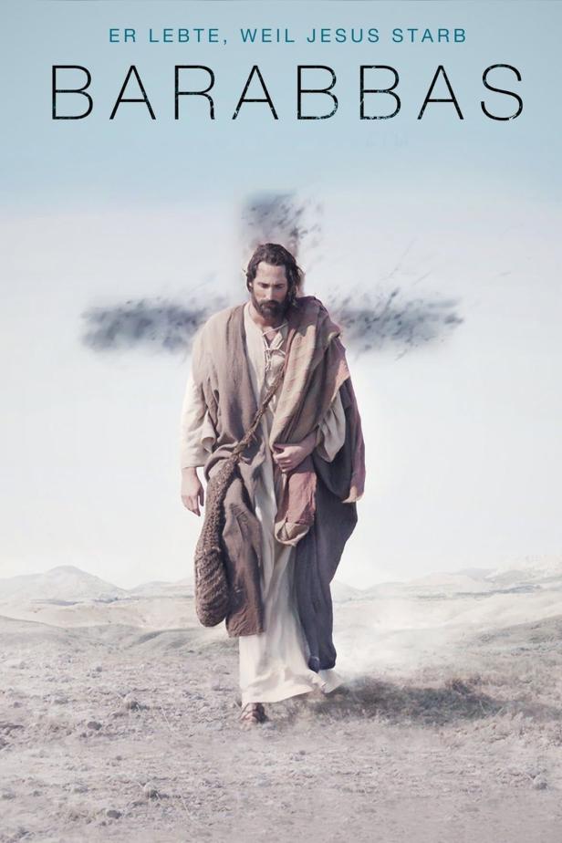 Ein Mann in traditioneller Kleidung geht vor einem Kreuz in einer Wüstenlandschaft.