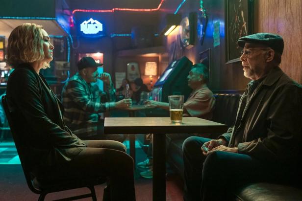 Eine Frau und ein älterer Mann sitzen an einem Tisch in einer Bar und unterhalten sich.