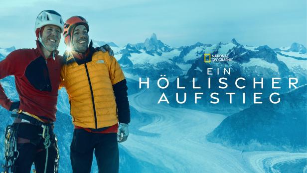 Zwei Bergsteiger umarmen sich vor einer verschneiten Berglandschaft.