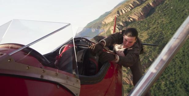 Tom Cruise hängt während eines Stunts an der Außenseite eines roten Flugzeugs in „Mission: Impossible“.