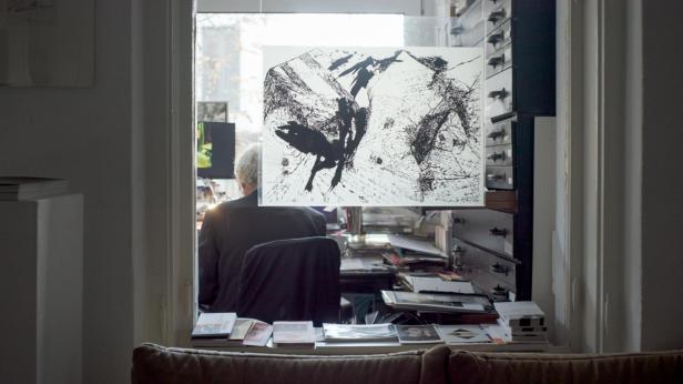 Ein Mann sitzt an einem Schreibtisch mit einer Zeichnung im Vordergrund.