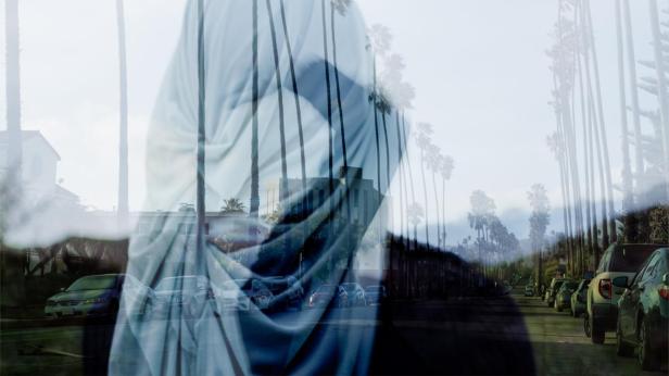 Eine Doppelbelichtung zeigt eine Person vor einer Straße mit Palmen und geparkten Autos.