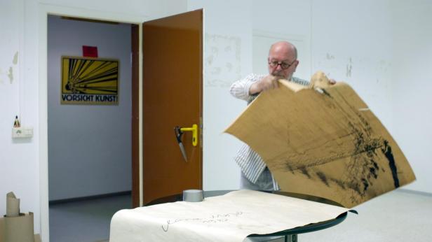 Ein Mann betrachtet eine Zeichnung in einem Raum mit einem „Vorsicht Kunst!“-Schild.