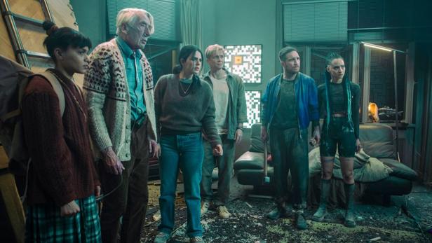 Eine Gruppe von sechs Personen steht in einem chaotischen Raum.