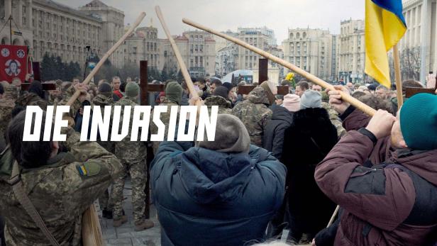 Eine Menschenmenge demonstriert mit Holzkreuzen und der ukrainischen Flagge gegen die Invasion.