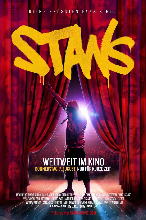 Ein Mann mit Kapuze steht auf einer Bühne vor dem Schriftzug „Stans“.