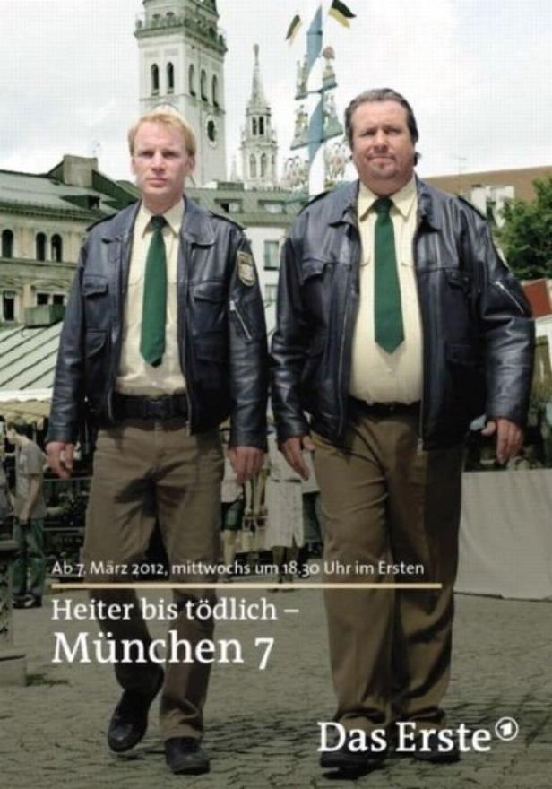 Zwei Polizisten in Lederjacken stehen vor dem Münchner Rathaus, Werbung für „Heiter bis tödlich – München 7“.
