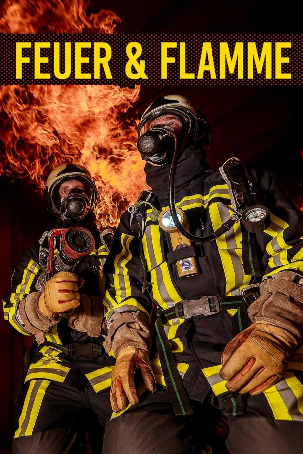 Zwei Feuerwehrleute in Schutzkleidung stehen vor einem Feuer.