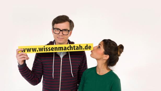 Ein Mann hält ein Schild mit der Aufschrift www.wissenmachtah.de, während eine Frau ihn zu küssen scheint.