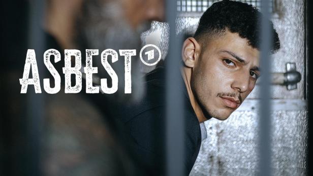 Ein junger Mann mit Verletzungen im Gesicht hinter Gittern, im Vordergrund der Titel „Asbest“.