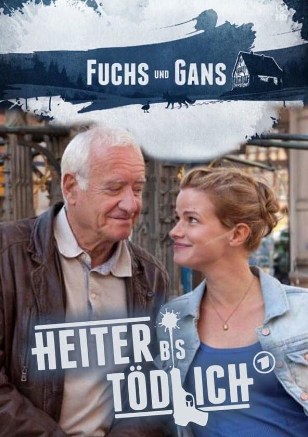Ein älterer Mann und eine jüngere Frau schauen sich auf dem Poster zu „Fuchs und Gans“ an.