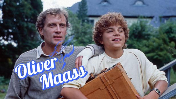 Ein Mann mit einem Jungen und einem Koffer vor einem Haus im Grünen.